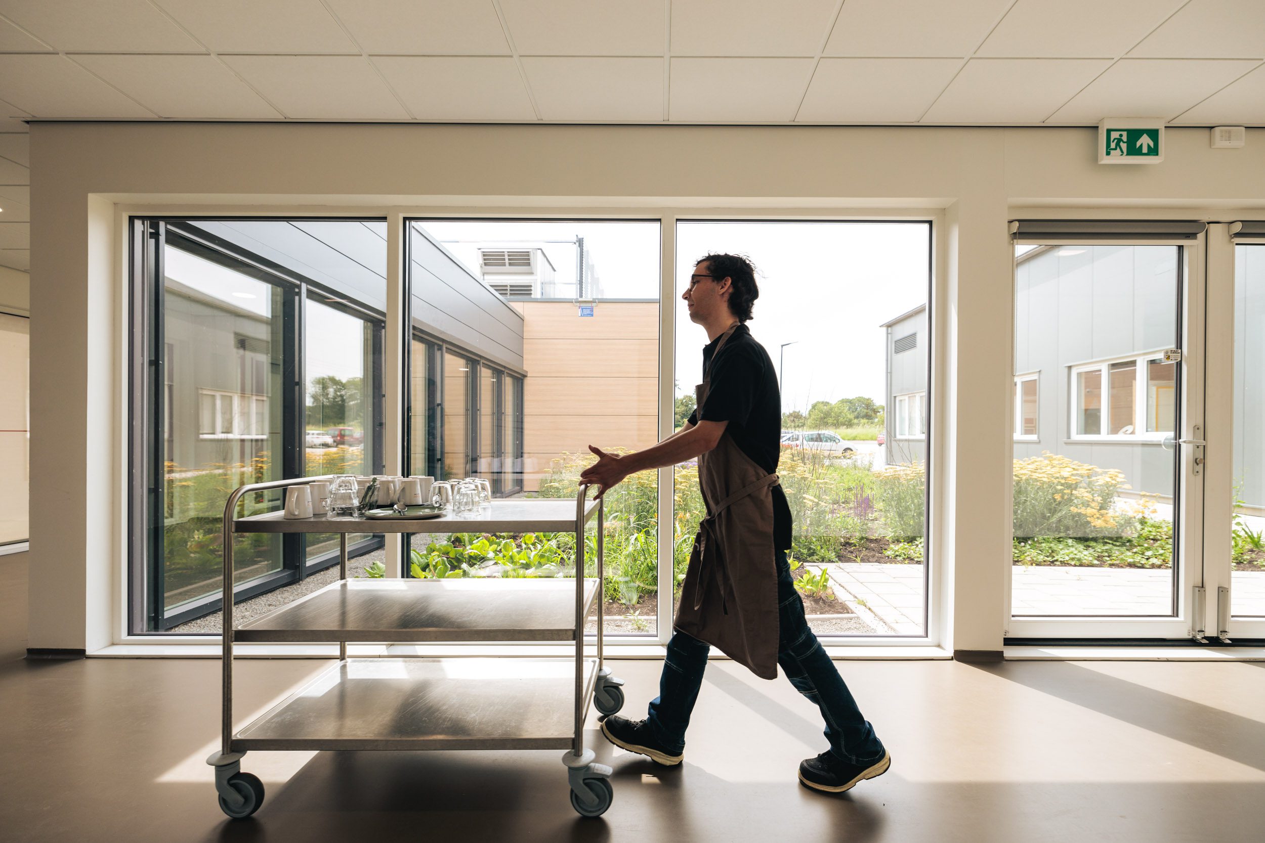 Een medewerker van het bedrijfsrestaurant van Afeer loopt door een gang. Door de glazen wand zie je de tuin.