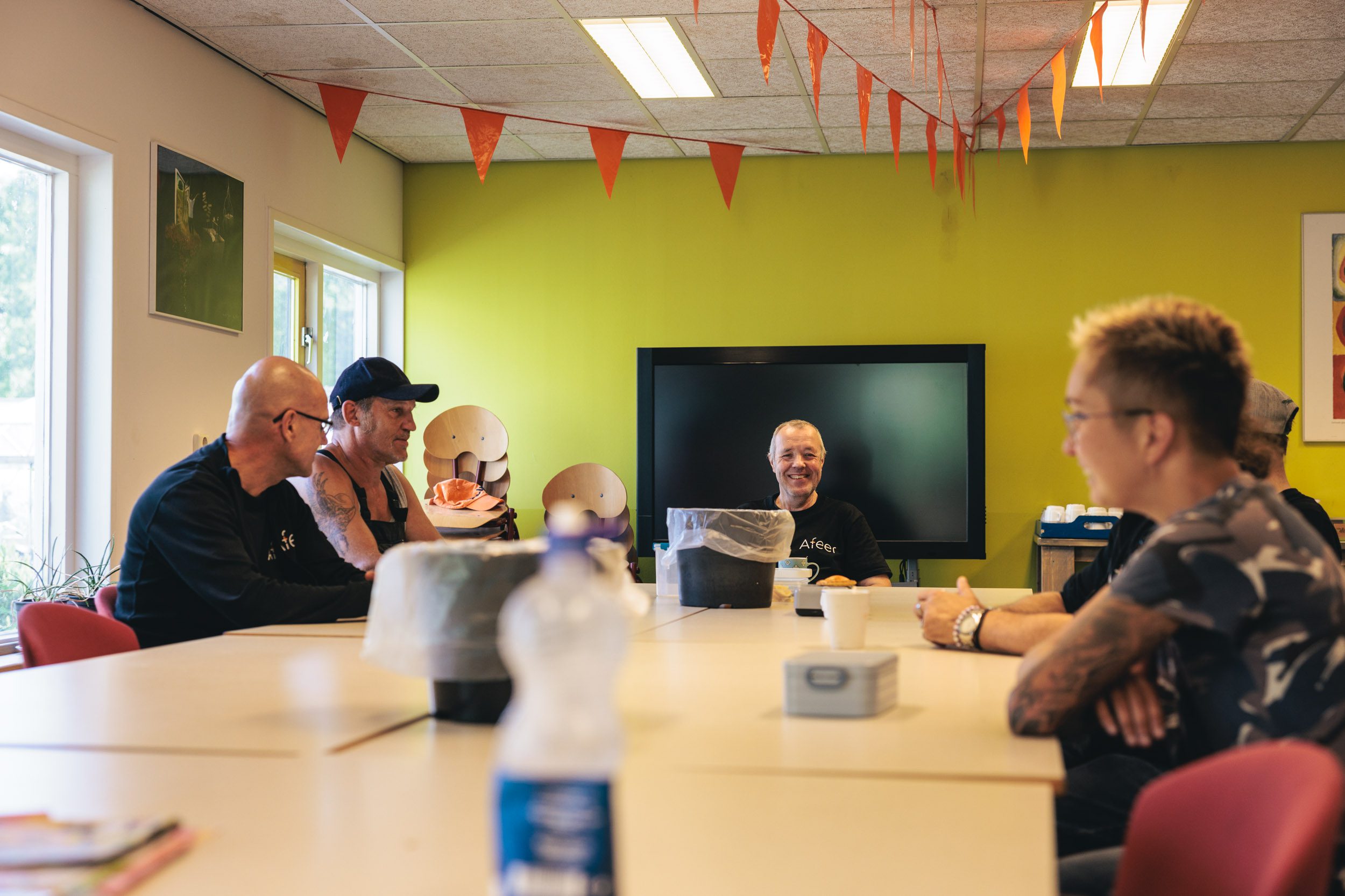 Medewerkers van Afeer in de kantine van Werklab Westerwolde. Aan het plafond hangen vlaggetjes.