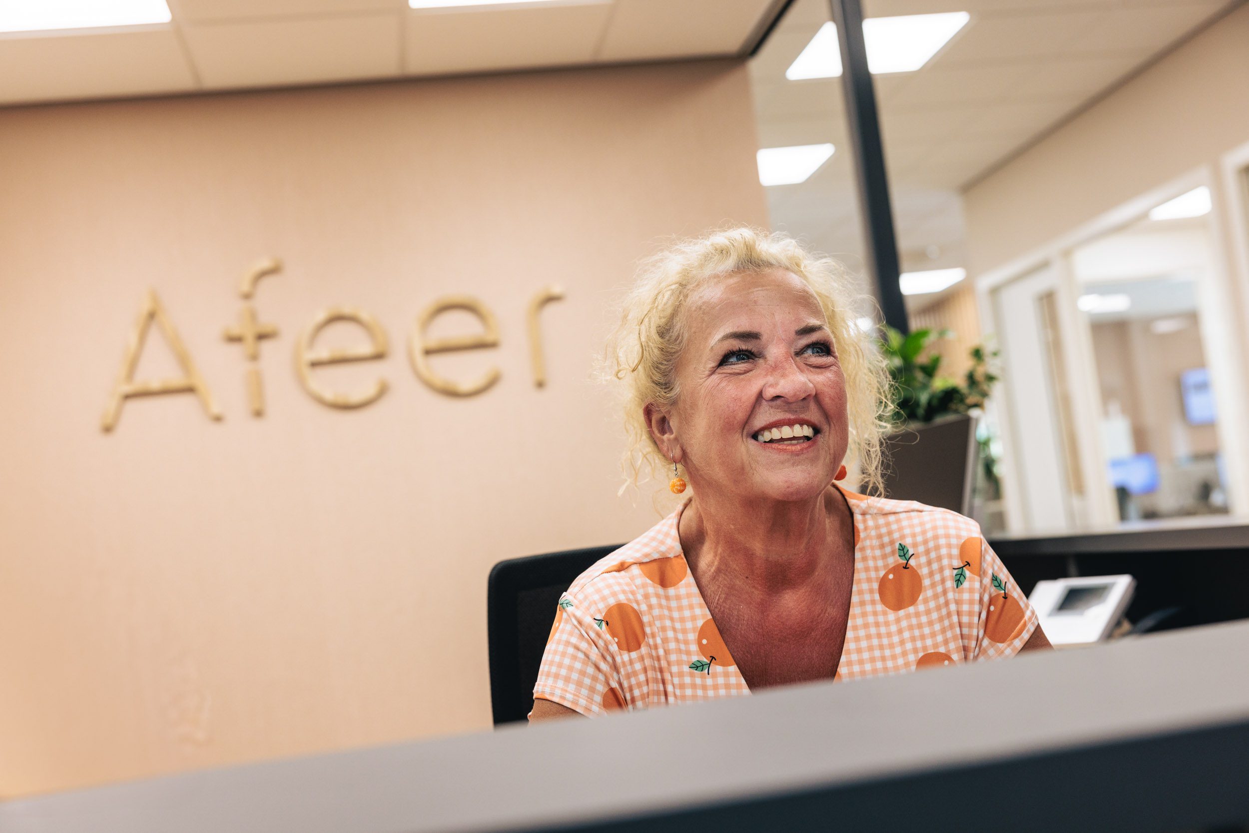 Een lachende receptioniste met op de achtergrond het logo van Afeer aan de muur