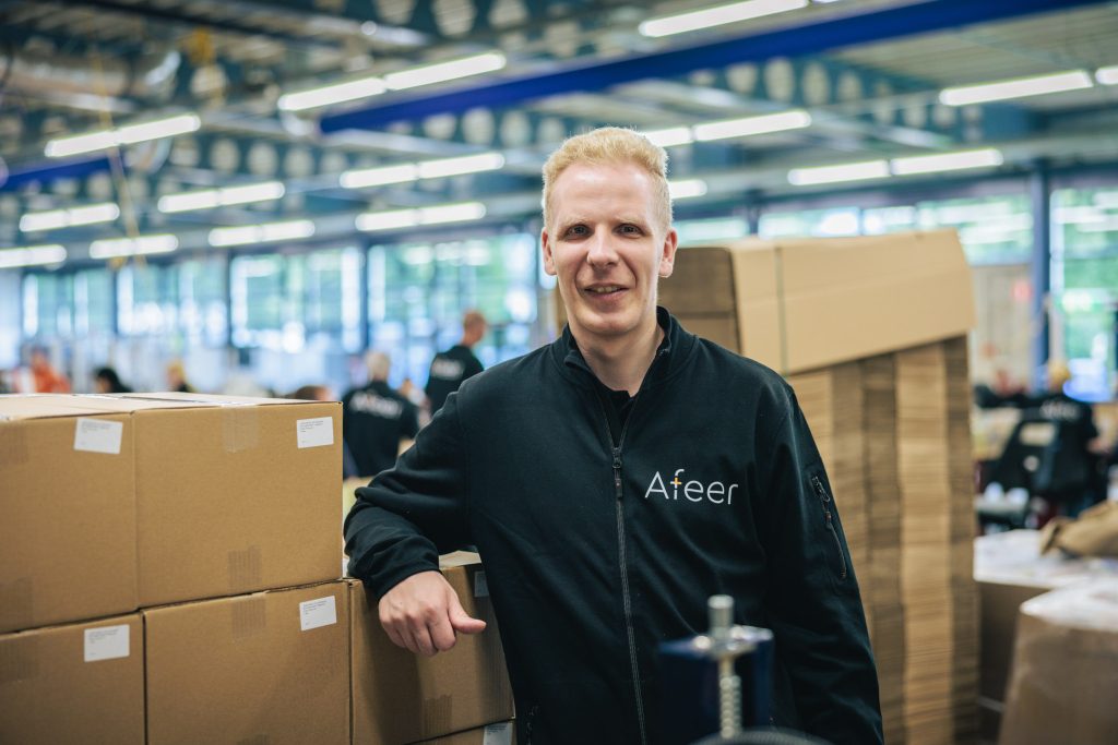 Een medewerker van Afeer staat bij een stapel dozen en kijkt lachend naar de camera