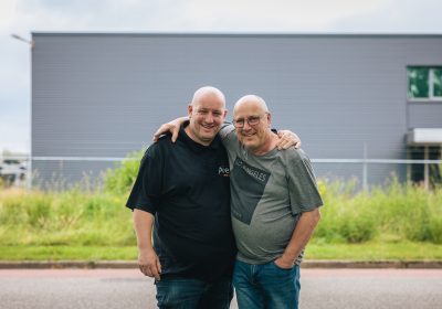 Twee mannen staan gearmd en lachen naar de camera