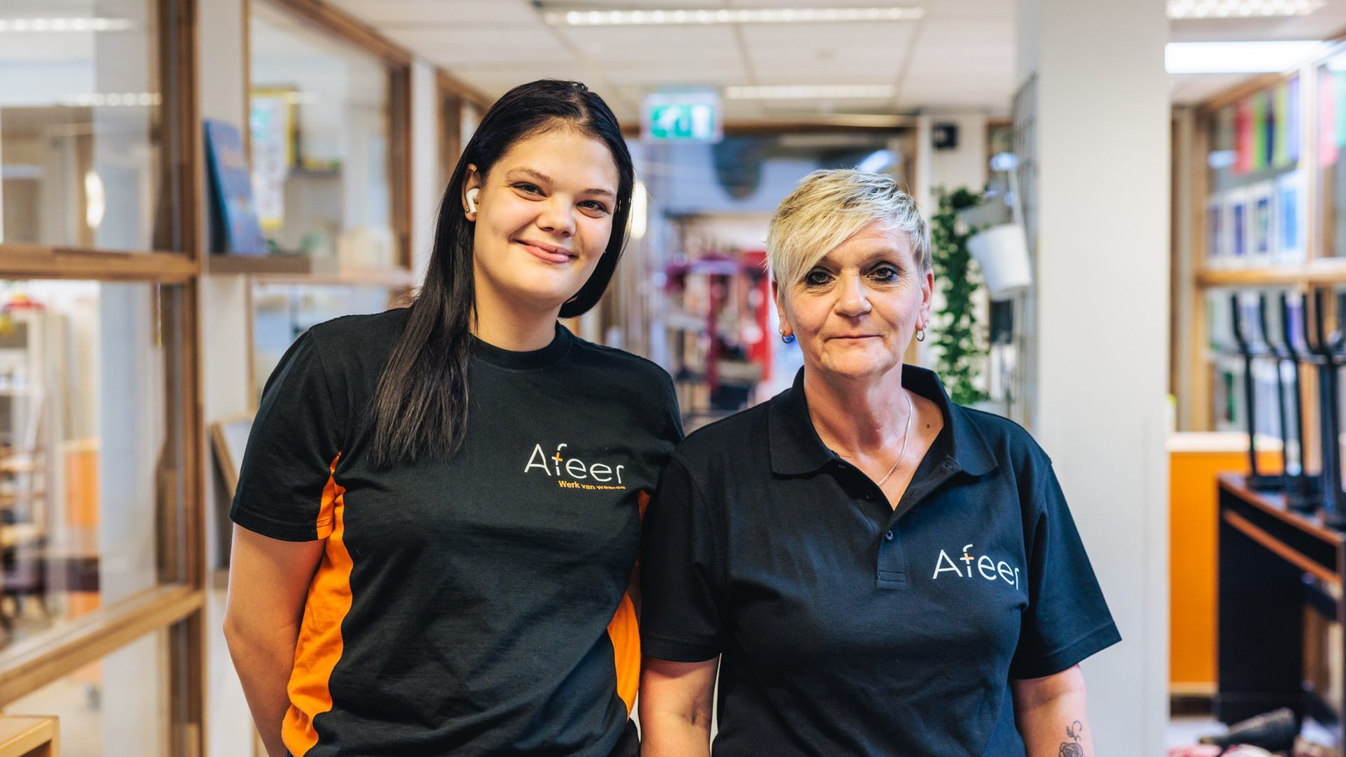 Twee schoonmaaksters van Afeer staan naast elkaar en lachen naar de camera